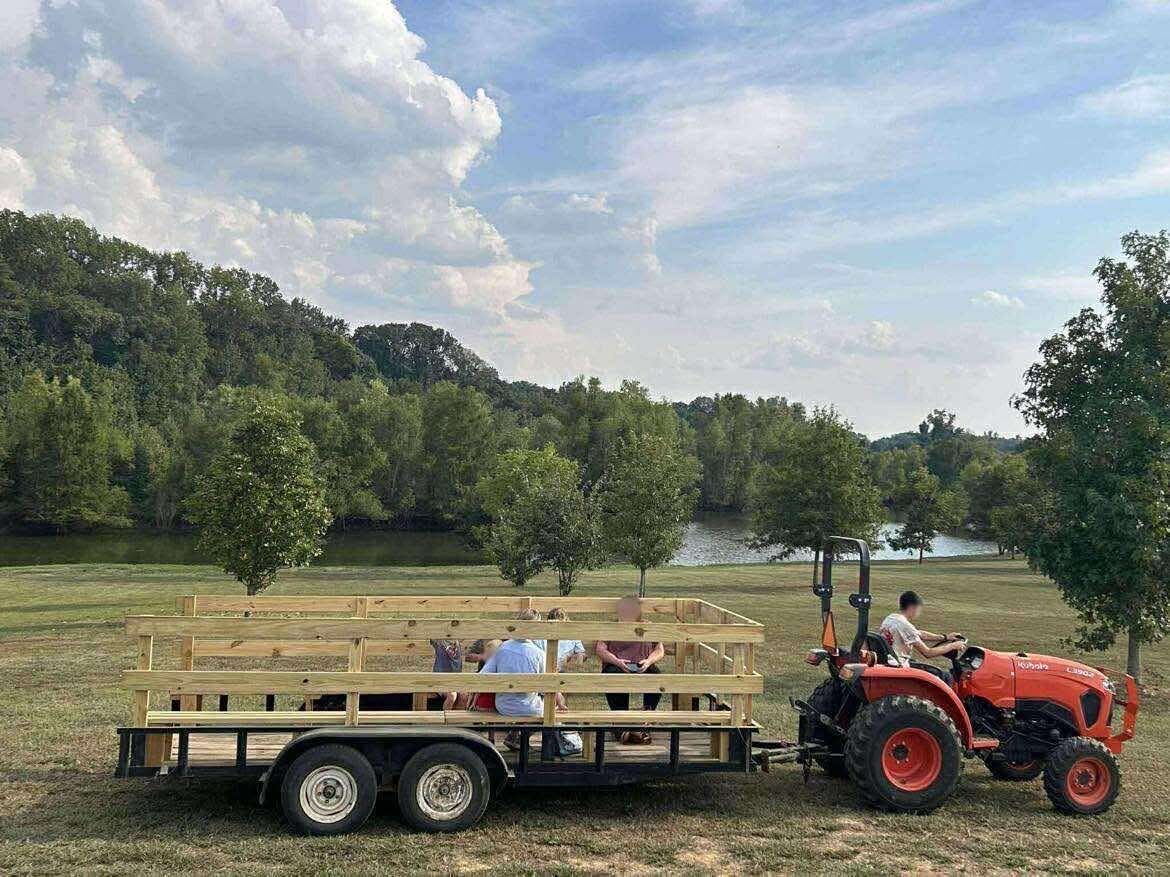 A red tractor pulling a hayride wagon beside a lake