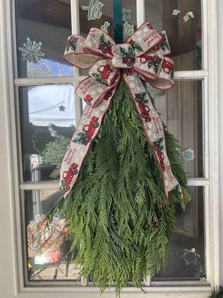 A garland swag with a red ribbon bow hanging on a door