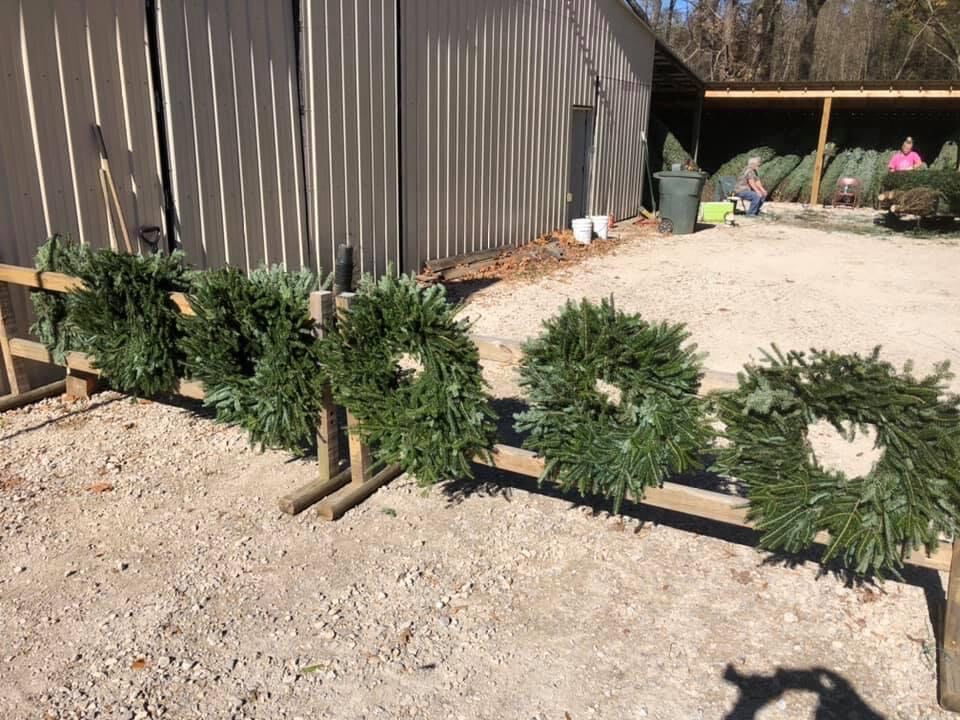 Fresh wreaths lined up on a rail beside a barn